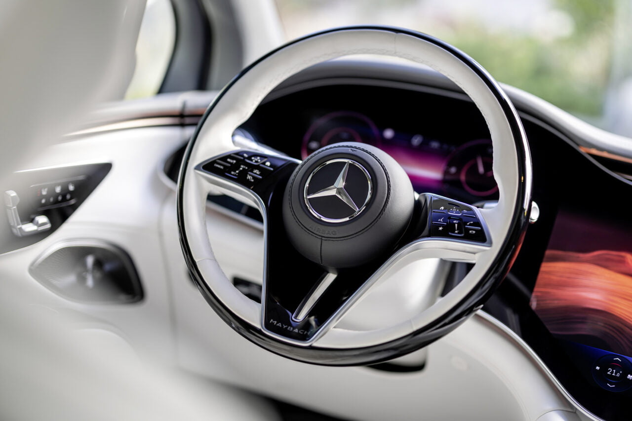 Wnętrze luksusowego samochodu z widoczną kierownicą z logo Mercedes-Benz, za kierownicą wyświetlacze z informacjami o aucie.