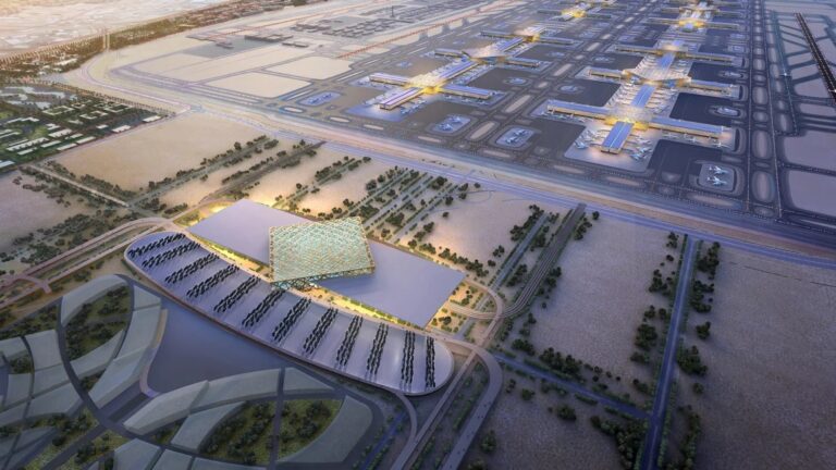 Widok z lotu ptaka na terminal lotniska o zmierzchu z iluminowanymi pasami startowymi, zaparkowanymi samolotami i infrastrukturą wspierającą.
