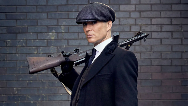 Mężczyzna w czarnym płaszczu i kapeluszu trzymający pistolet maszynowy na tle ceglanej ściany.