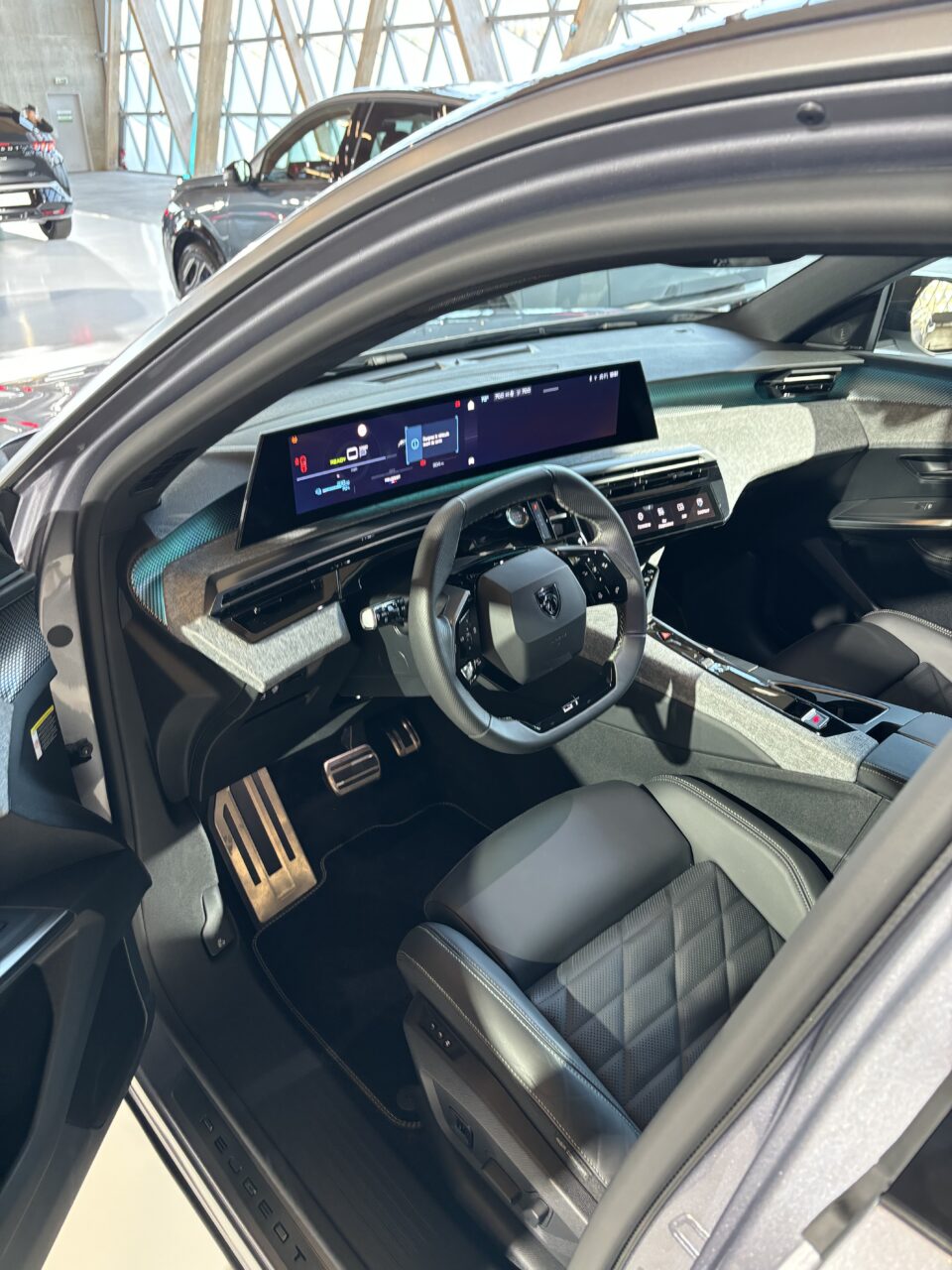 Wnętrze nowoczesnego samochodu z widoczną konsolą środkową, kierownicą z logo producenta, wyświetlaczem cyfrowym i skórzanymi siedzeniami.