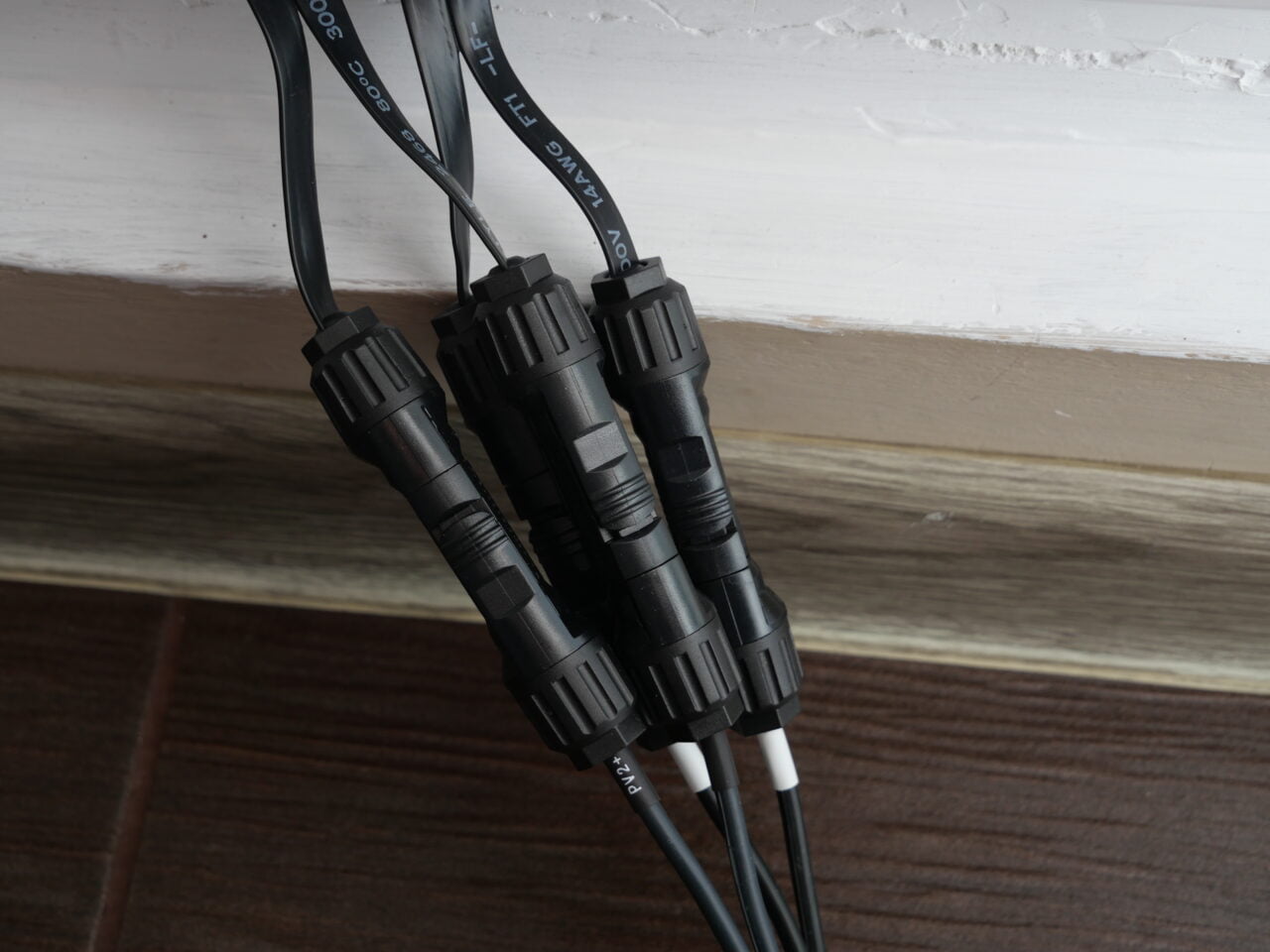Czarne złącza kablowe na drewnianej podłodze przy ścianie.