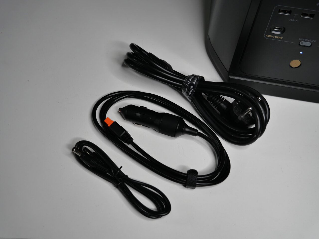 Kable zasilające na białym tle obok częściowo widocznego UPS-a ze złączami USB i prądem zmiennym.