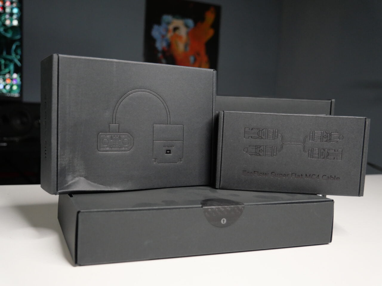 Czarne, eleganckie pudełka z nadrukowanymi rysunkami produktów elektronicznych, ułożone na biurku.