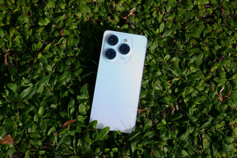 Smartfon z potrójnym aparatem leżący na zielonych liściach.