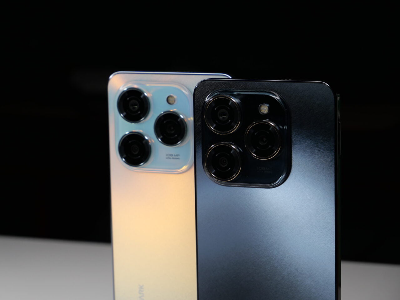 Dwa smartfony ustawione tyłem z widocznymi aparatami z czterema obiektywami, jeden w kolorze błękitno-złotym, drugi w czarno-szarym.
