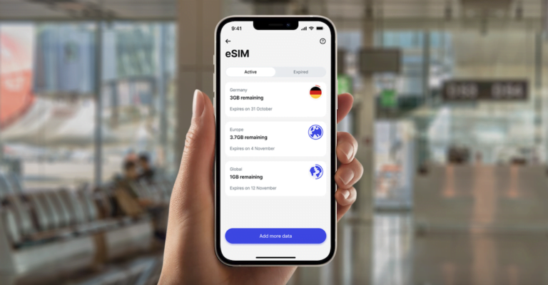 Ręka trzymająca smartfon z otwartą aplikacją eSIM wyświetlającą aktywne plany danych dla Niemiec, Europy i globalnego zasięgu, z informacjami o pozostałej ilości danych i datami wygaśnięcia. Tło rozmyte, prawdopodobnie wnętrze lotniska.