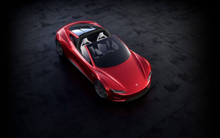 Tesla Roadster - czerwony samochód sportowy marki Tesla z otwartym szklanym dachem zaparkowany na ciemnoszarej, betonowej nawierzchni.