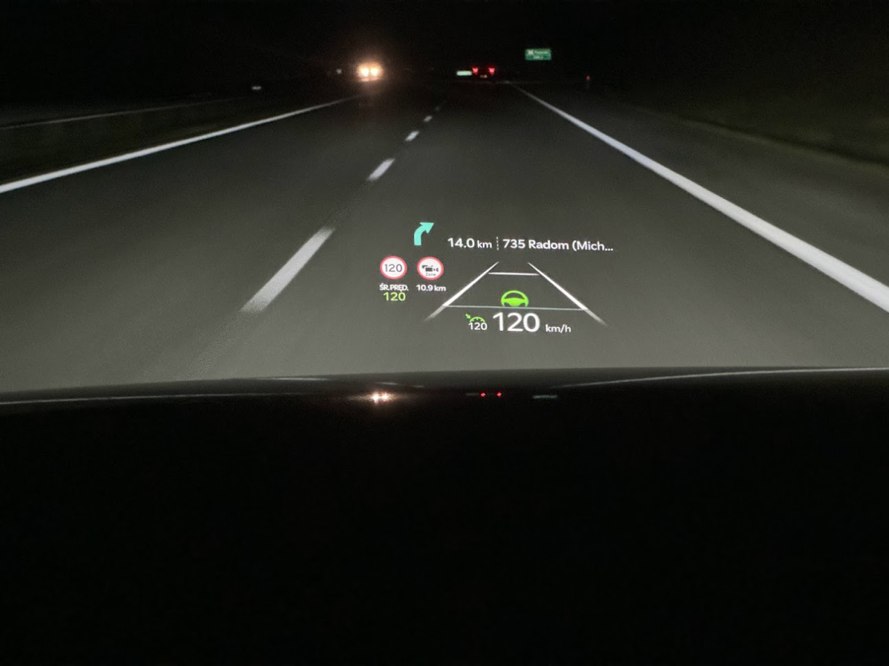 Nocna jazda samochodem z włączonym systemem head-up display pokazującym informacje nawigacyjne i prędkość pojazdu na przedniej szybie.