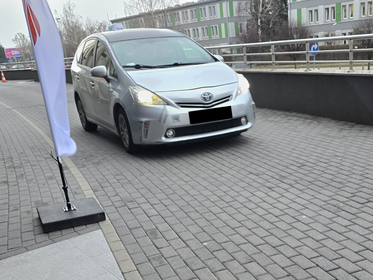 Szary samochód marki Toyota, taksówka UberX Share, stoi na bruku obok białej flagi z logotypem.
