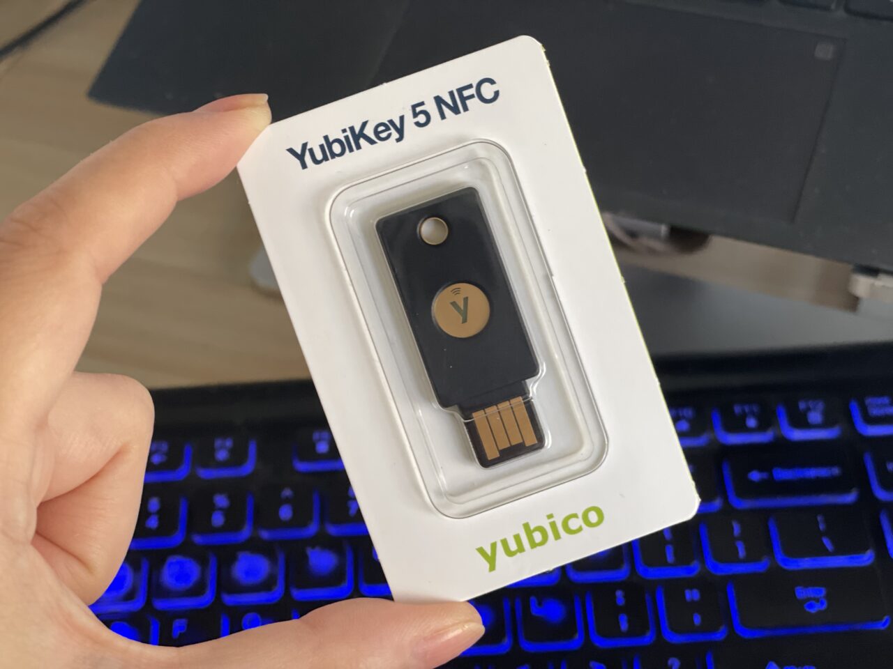 Opakowanie zabezpieczeń YubiKey 5 NFC na dłoni przed klawiaturą komputera.