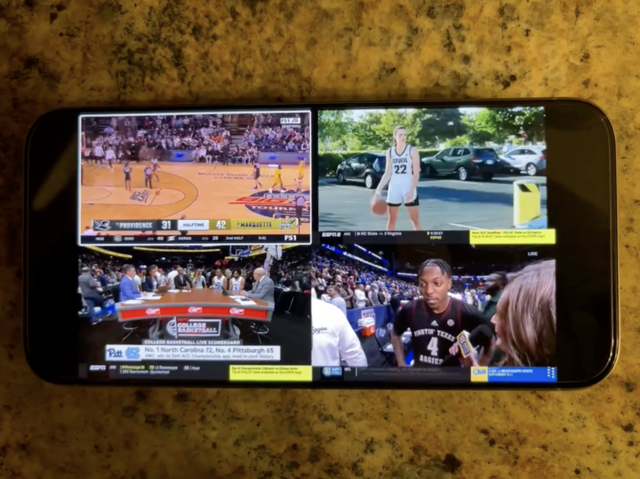 Smartfon wyświetlający podzielony ekran z czterema różnymi transmisjami sportowymi, w tym koszykówkę i wywiad z koszykarzem.