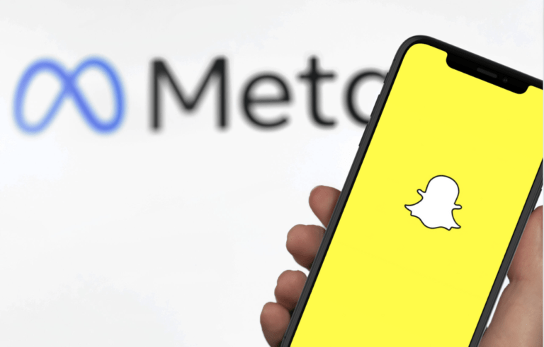 Ręka trzymająca smartfon z ekranem wyświetlającym logo aplikacji Snapchat, w tle rozmyty napis "Meta".