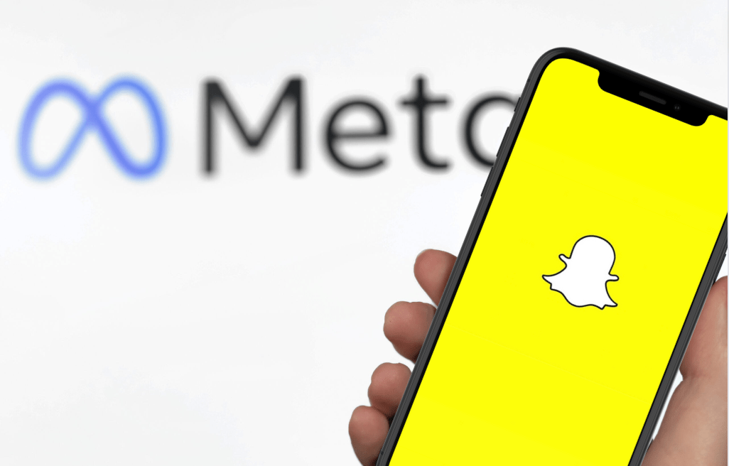 Ręka trzymająca smartfon z ekranem wyświetlającym logo aplikacji Snapchat, w tle rozmyty napis "Meta".
