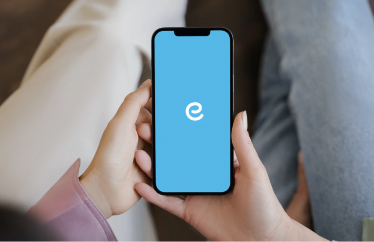 Osoba trzyma smartfon z niebieskim ekranem wyświetlającym literę "e" na środku.