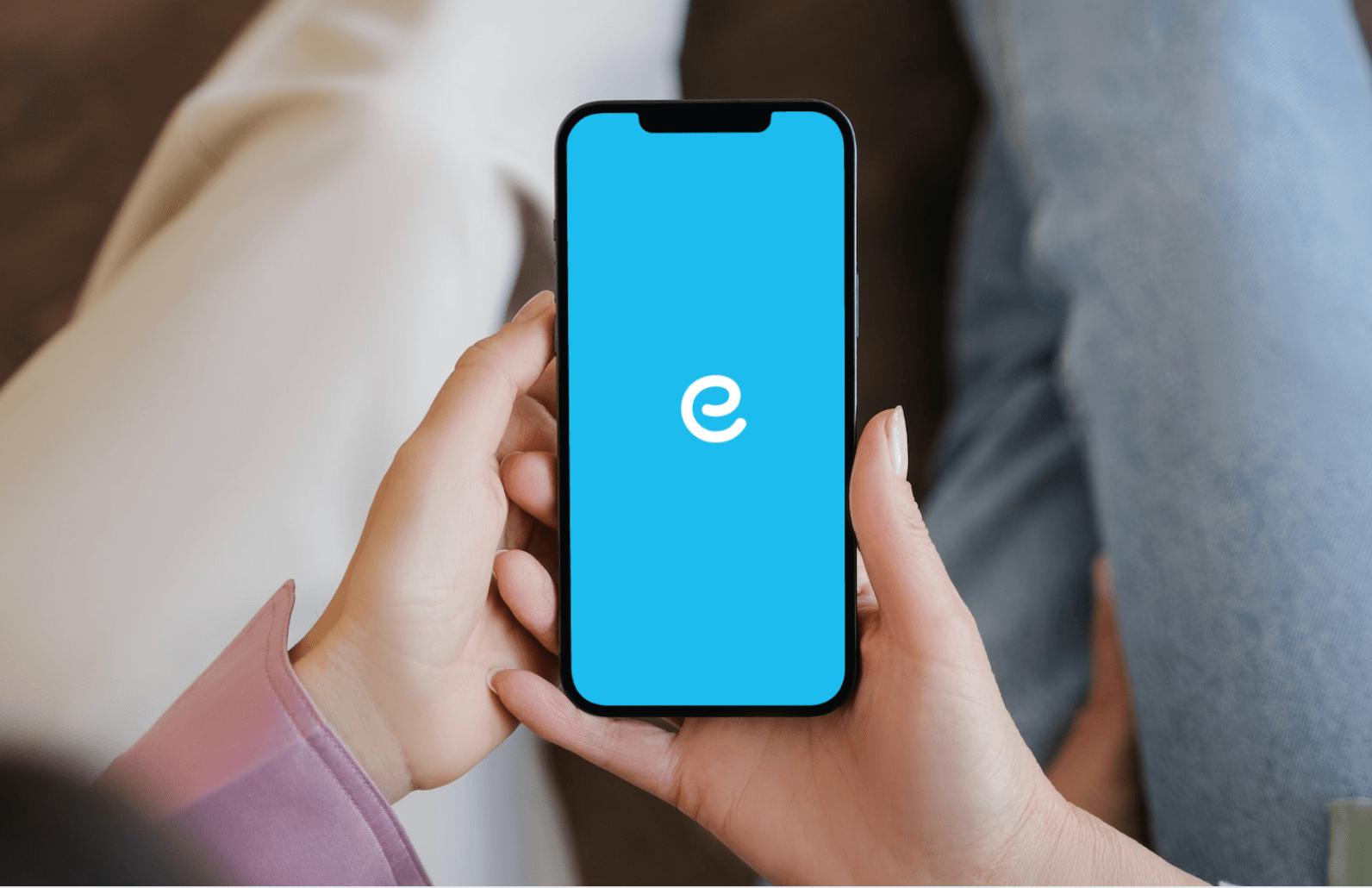 Osoba trzyma smartfon z niebieskim ekranem wyświetlającym literę "e" na środku.