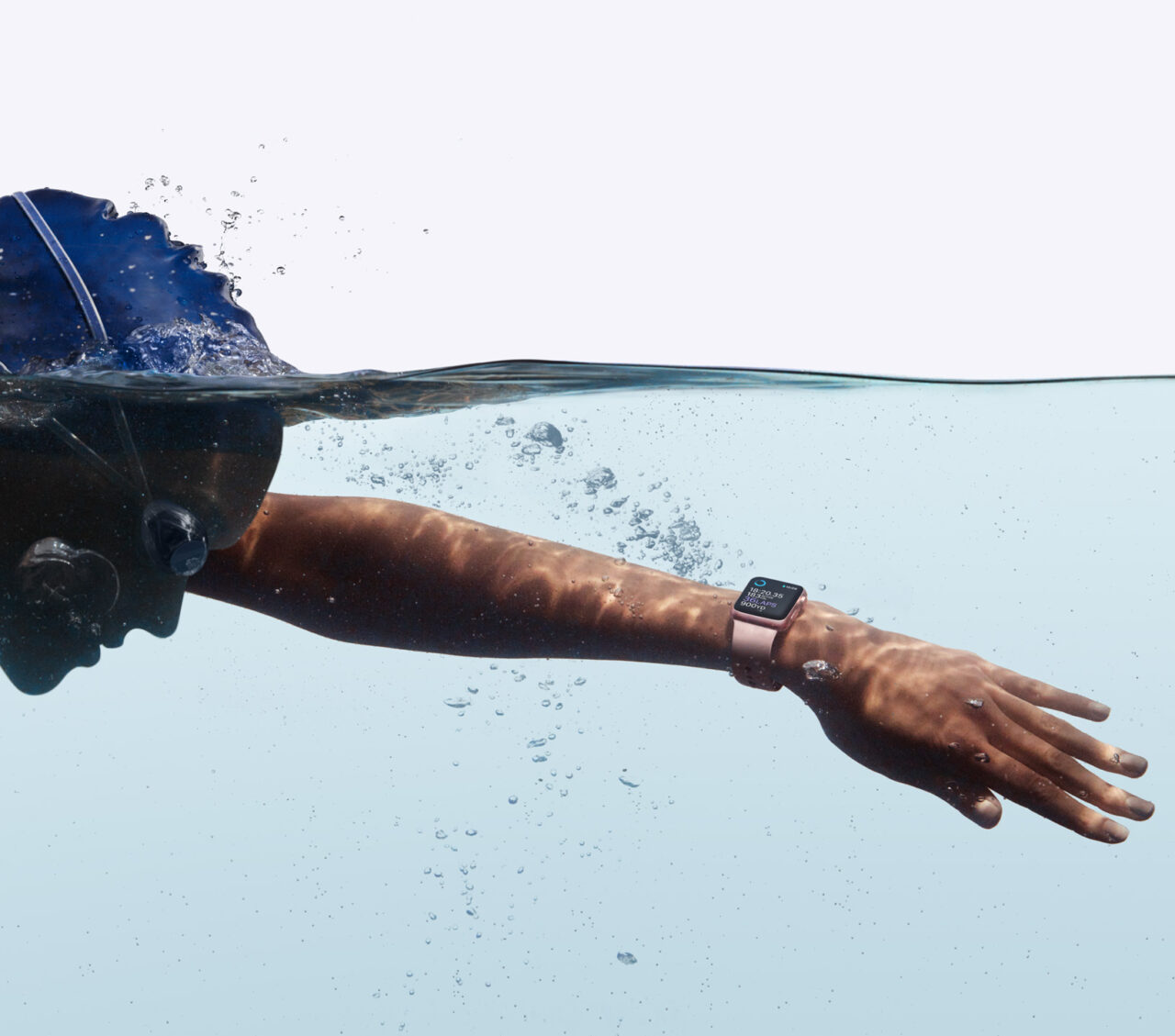 Pływak w trakcie przeciągnięcia ręki pod wodą, z zegarkiem na nadgarstku; widok zarówno powyżej, jak i poniżej powierzchni wody.