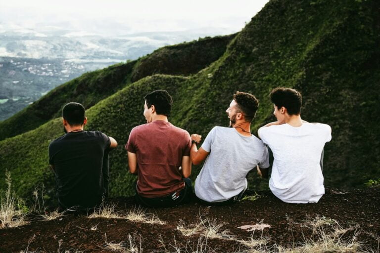 Czterech mężczyzn świętujących Dzień Mężczyzn, siedzących plecami na wzgórzu i patrzących na zielony krajobraz.