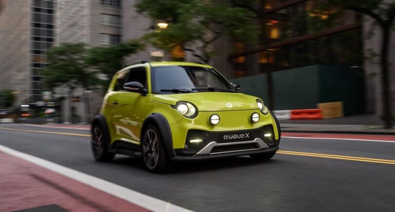 Zielony, elektryczny samochód miejski marki e.go poruszający się po miejskiej drodze z rozmytym tłem, pokazujący ruch i dynamikę jazdy.