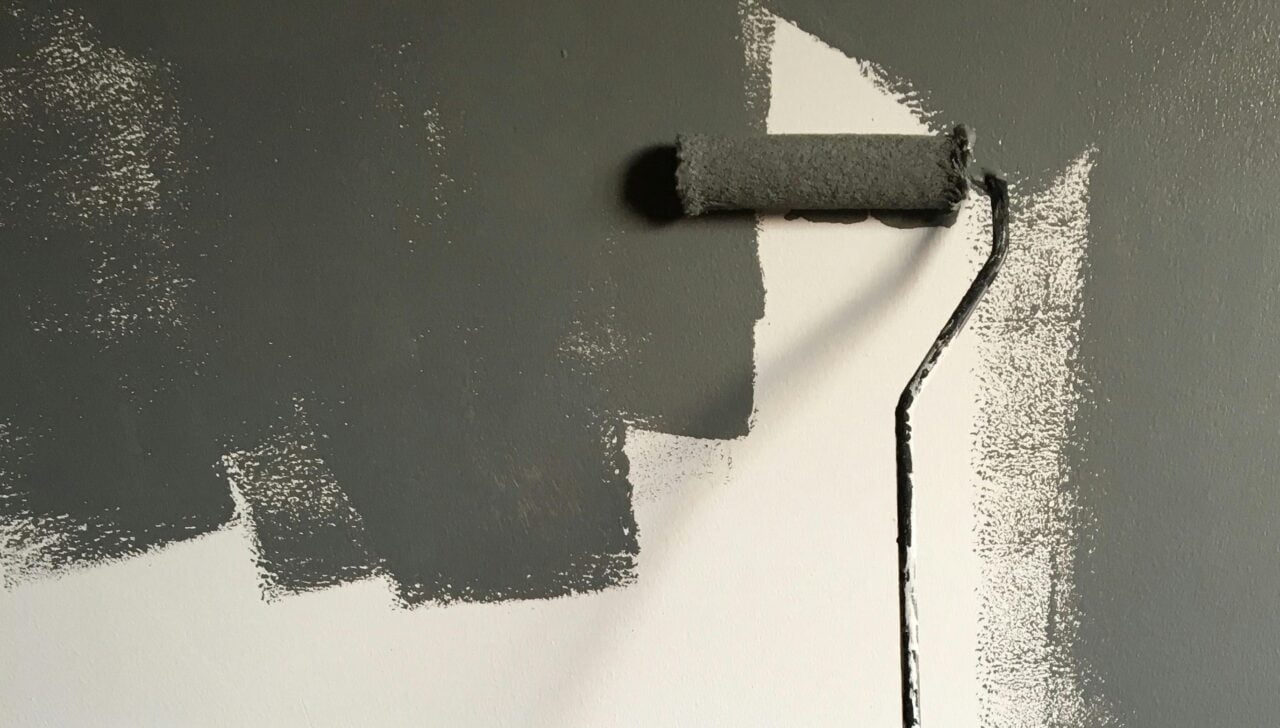 Wałek malarski malujący szarą farbą fotowoltaiczną naścienną na białej ścianie.