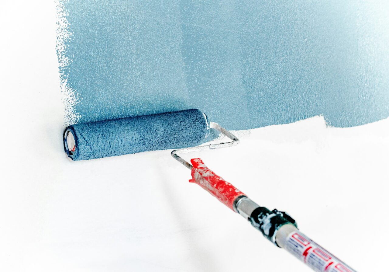 Wałek malarski malujący ścianę farbą fotowoltaiczną na niebiesko, częściowo pomalowana powierzchnia.