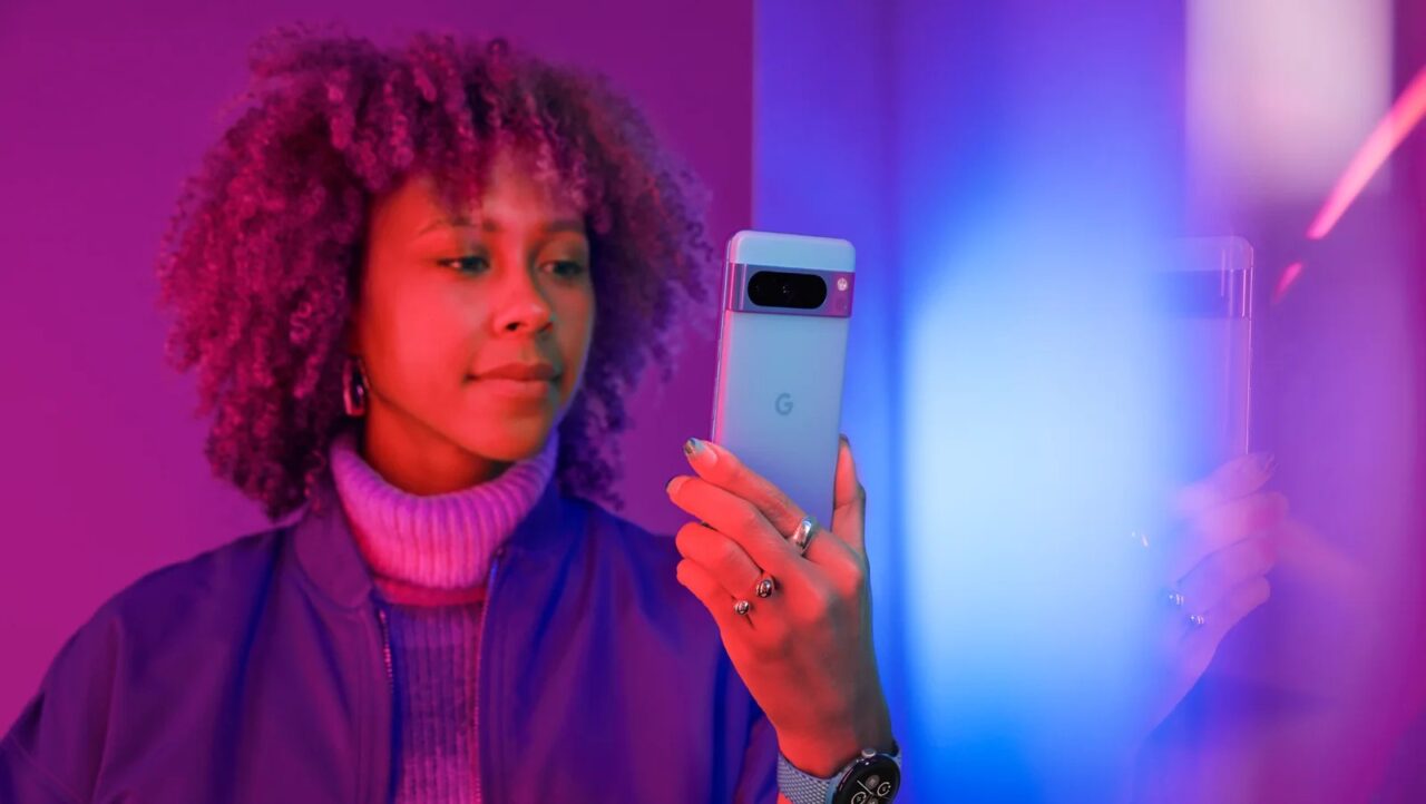 Google pixel 8a. Kobieta trzymająca smartfon w dłoni, w pomieszczeniu z różowo-niebieskim oświetleniem LED.