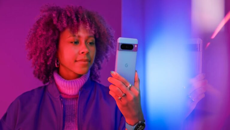 Kobieta trzymająca nowoczesny smartfon w dłoni na tle różowo-niebieskiego oświetlenia.