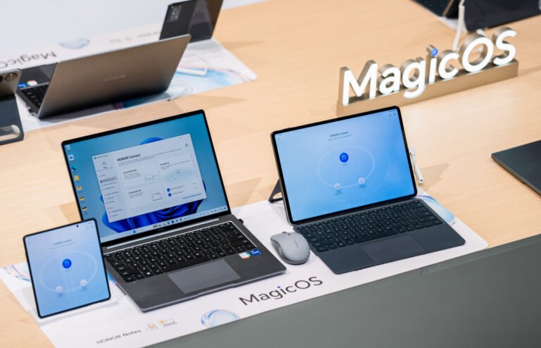 Stoisko z urządzeniami elektronicznymi z wyeksponowanym napisem "MagicOS", w tym laptopami, tabletem i smartfonem, przedstawiającymi interfejs użytkownika.