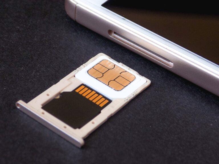 Karta SIM leżąca obok wnęki na kartę w smartfonie na czarnym tle.