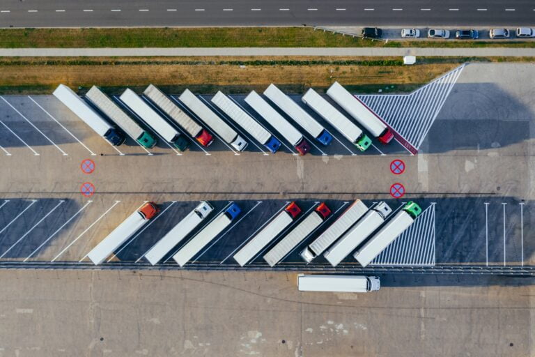 Zdjęcie z lotu ptaka przedstawiające zaparkowane ciężarówki wzdłuż doków załadunku, z drogą przebiegającą po lewej stronie.