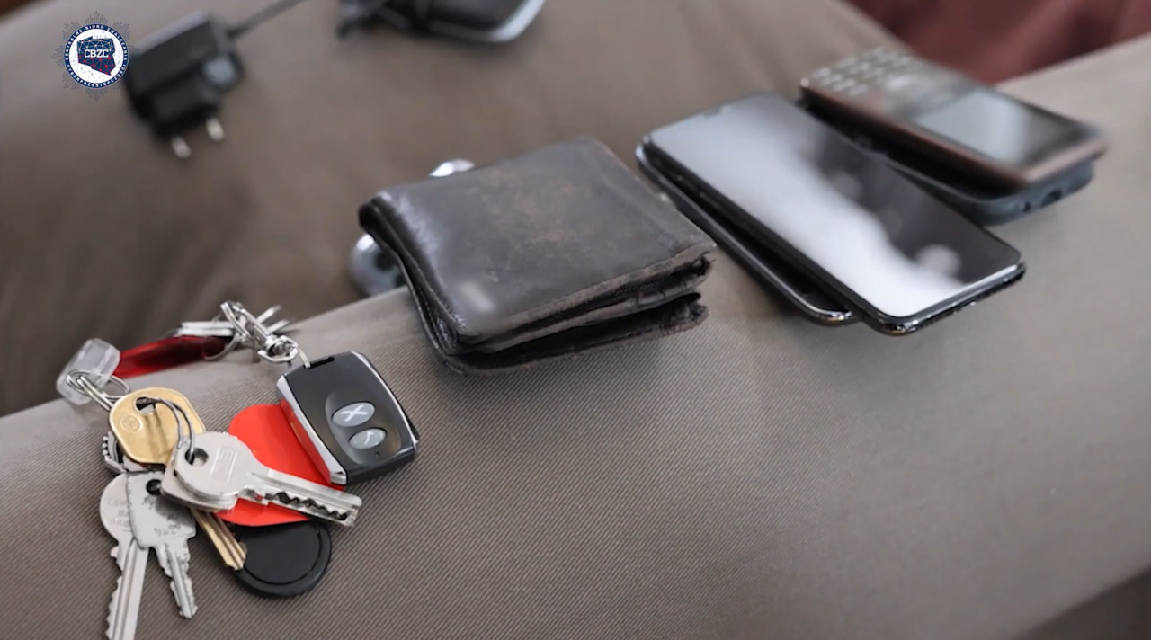 Zestaw przedmiotów codziennego użytku na sofie: klucze, portfel i dwa smartfony.