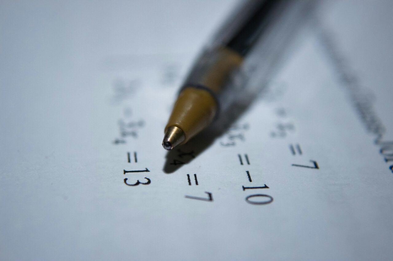 Nauczyciel, który odłożył długopis leżący na arkuszu papieru z wydrukowanymi działaniami matematycznymi, skupienie na końcówce długopisu.