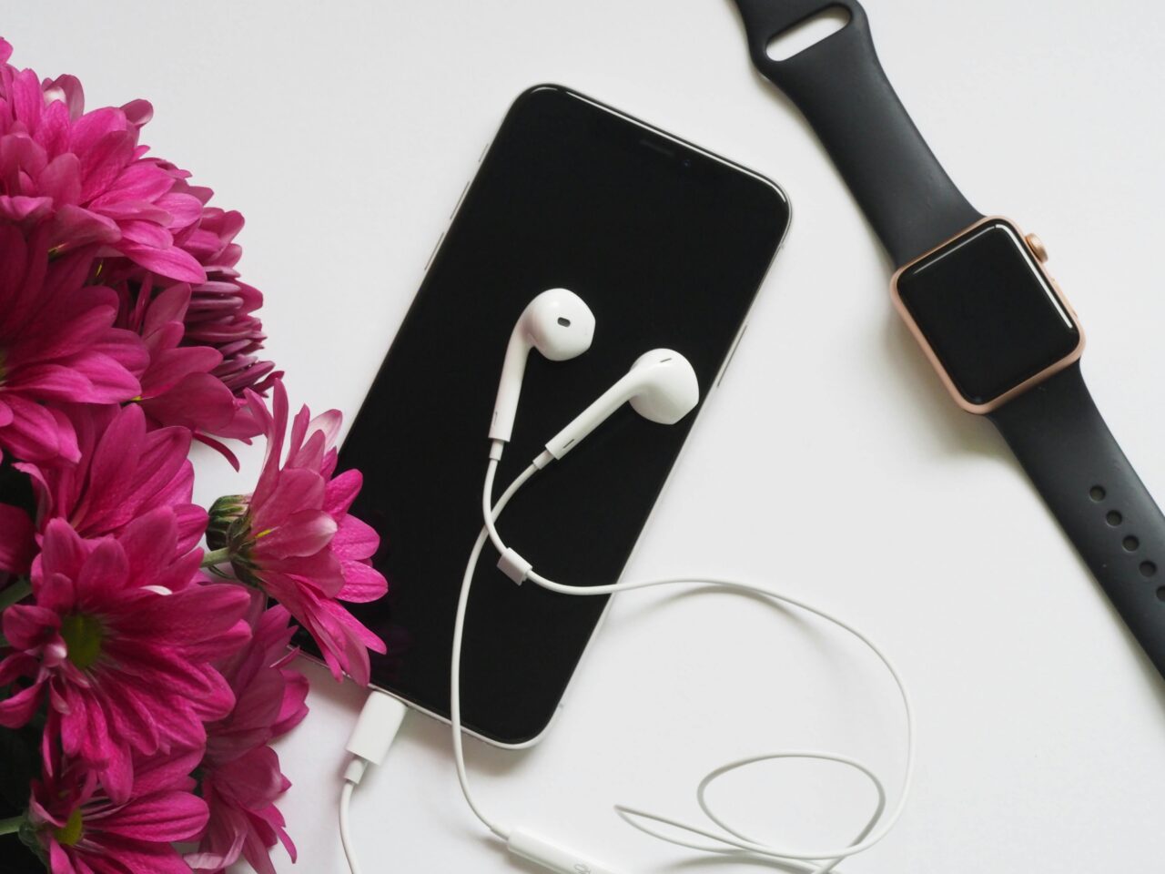 Nagrywanie ekranu iPhone. Czarne smartfon i smartwatch obok różowych kwiatów i białych słuchawek na białym tle.