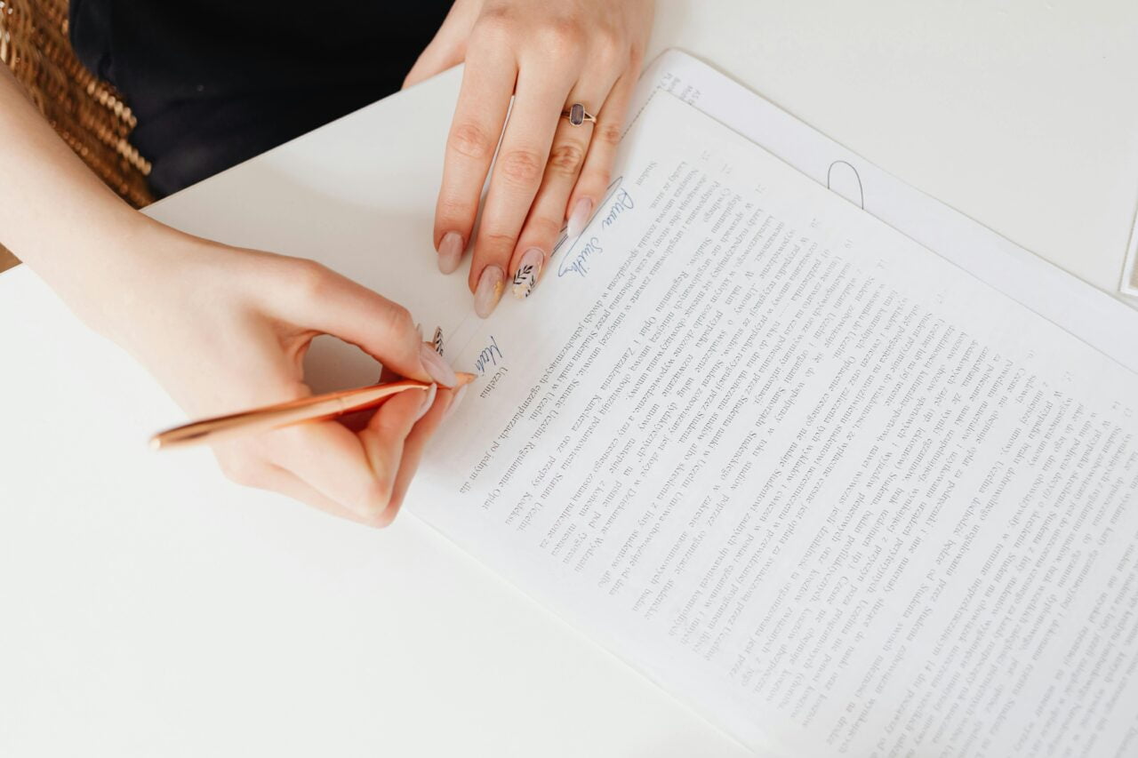 Osoba koryguje tekst na wydrukowanym dokumencie, trzymając długopis w dłoni.