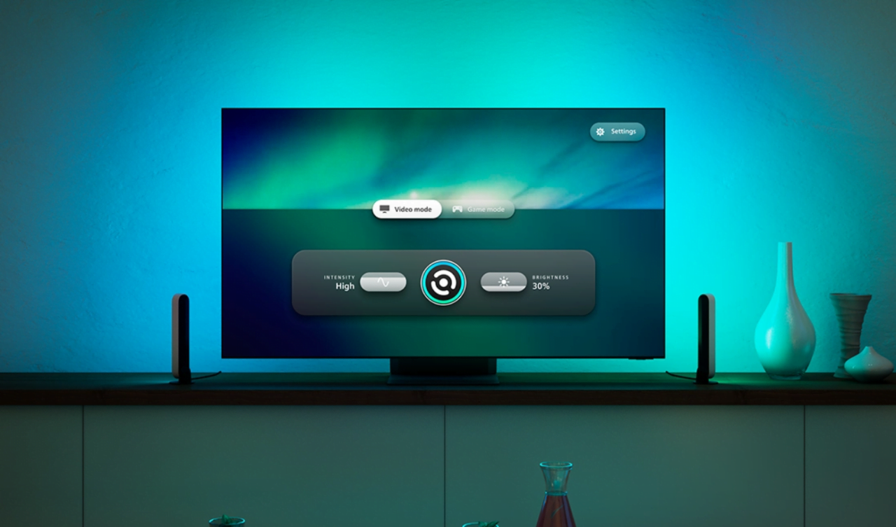 Telewizor z płaskim ekranem na drewnianej szafce, otoczony przez kolorowe oświetlenie LED, wyświetla menu ustawień obrazu na tle abstrakcyjnej grafiki. Obok telewizora dwie minimalistyczne dekoracyjne wazy.