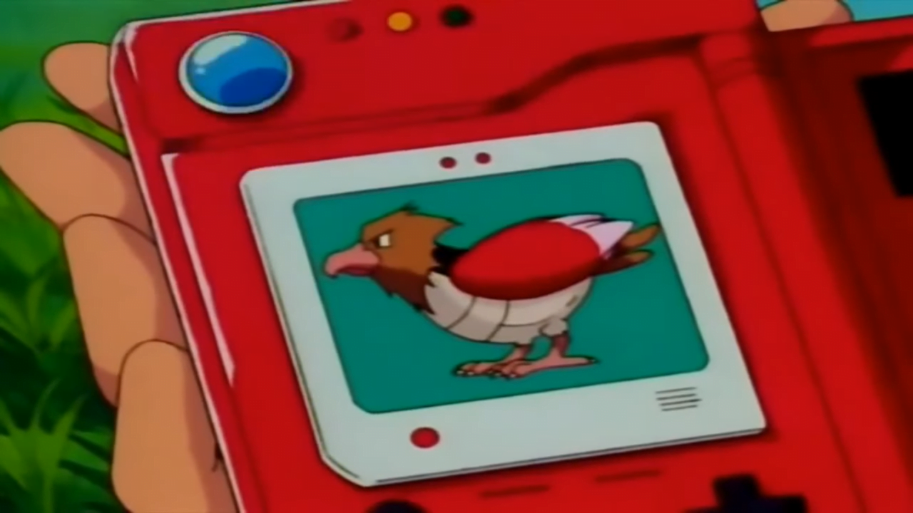 Czerwone urządzenie elektroniczne z ilustracją ptaka na ekranie, trzymane w dłoni, z zielonym tłem.