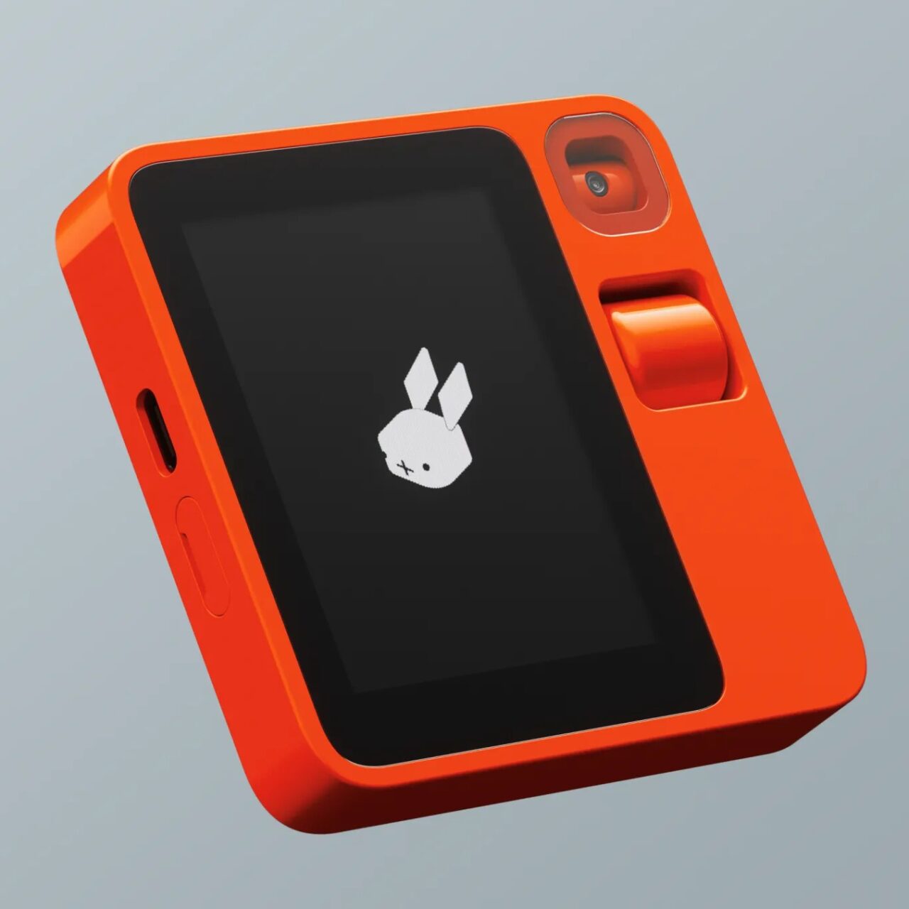 Pomarańczowy Rabbit R1 z wyświetlaczem pokazującym logo z białym króliczkiem na szarym tle i wbudowanym obiektywem aparatu.