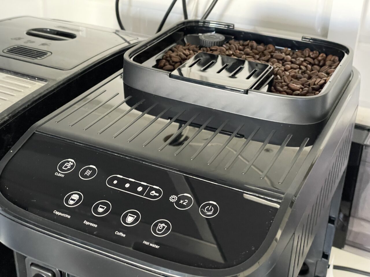 Czarny ekspres do kawy z otwartym pojemnikiem na ziarna kawy i dotykowym panelem sterowania z ikonami różnych napojów kawowych.
