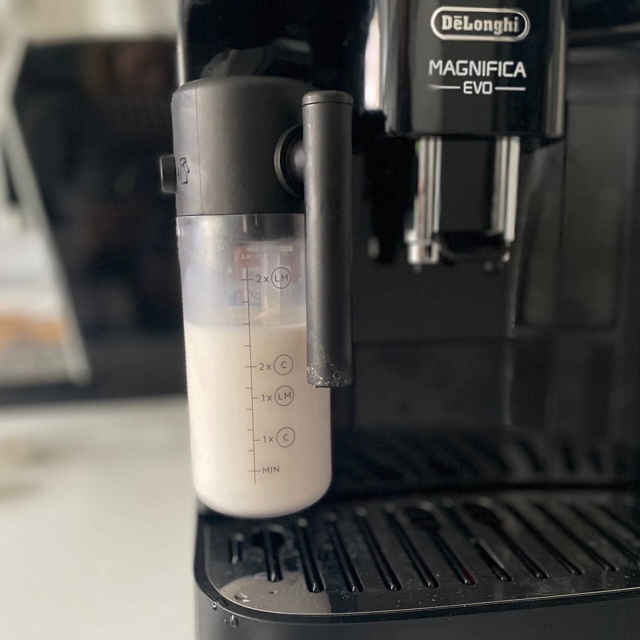Ekspres do kawy marki DeLonghi, model Magnifica EVO, z widocznym pojemnikiem na mleko.