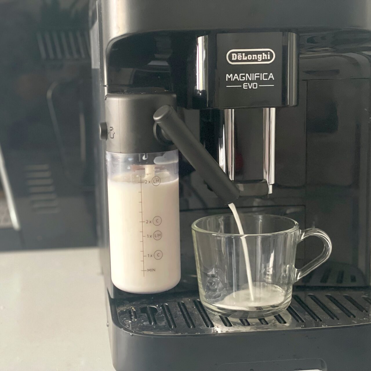 Ekspres do kawy De'Longhi Magnifica EVO z wbudowanym spieniaczem mleka napełniającym szklankę mlekiem.