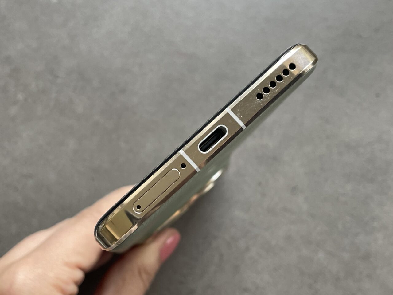 Złoty smartphone z widocznym gniazdem USB, głośnikiem i złączem słuchawkowym na szarym tle.