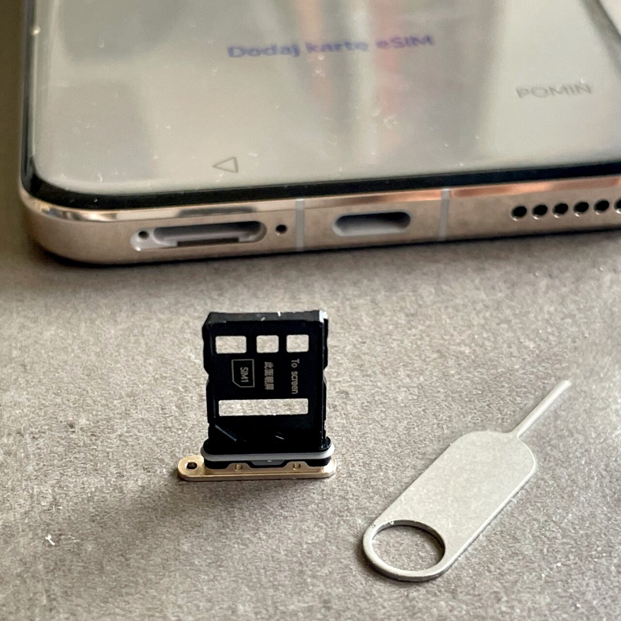 Zdjęcie smartfona z otwartą szufladką na karty SIM i eSIM oraz leżącą obok metalową kluczyk do wyjmowania szufladki.