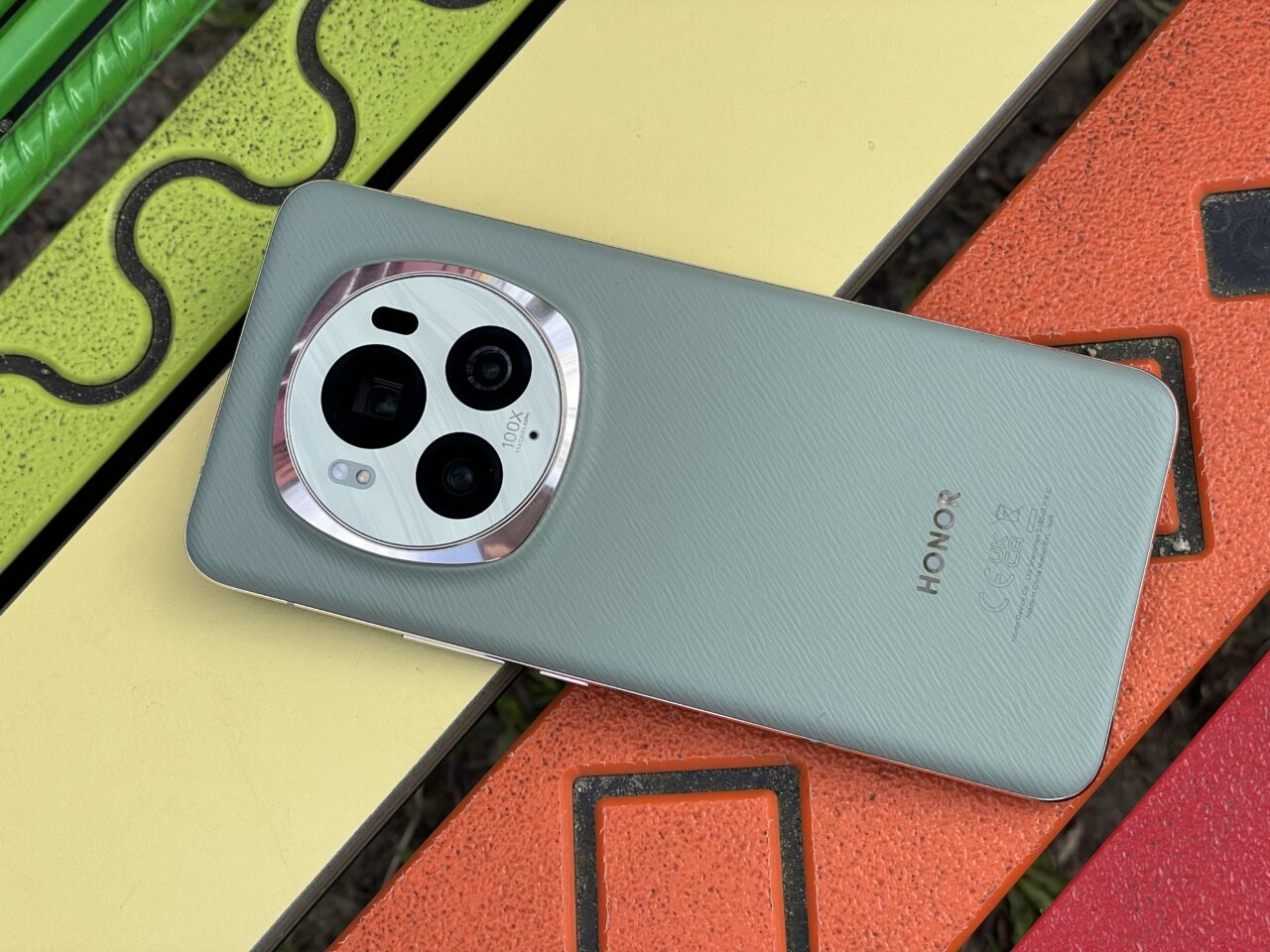 Smartfon marki Honor leżący na ławce, z tylnym aparatem fotograficznym o kształcie okręgu i napisem "100x Zoom".