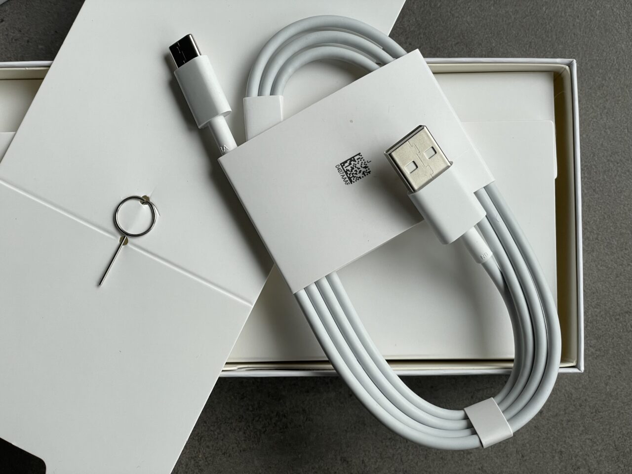Biały kabel USB-C do USB-A oraz narzędzie do otwierania tacki karty SIM, ułożone na pudełku.