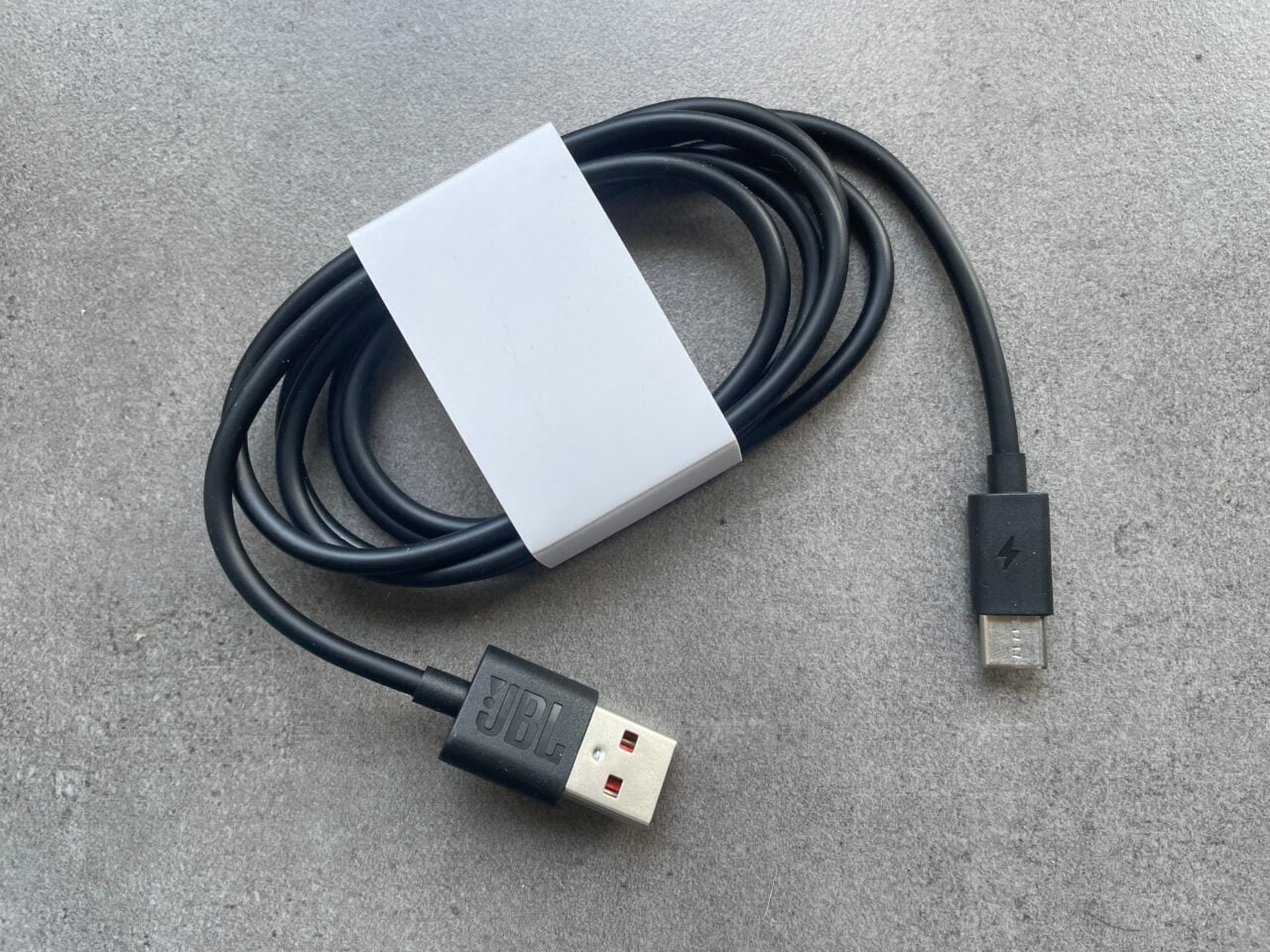 Czarny kabel USB z białą ładowarką na szarym tle.