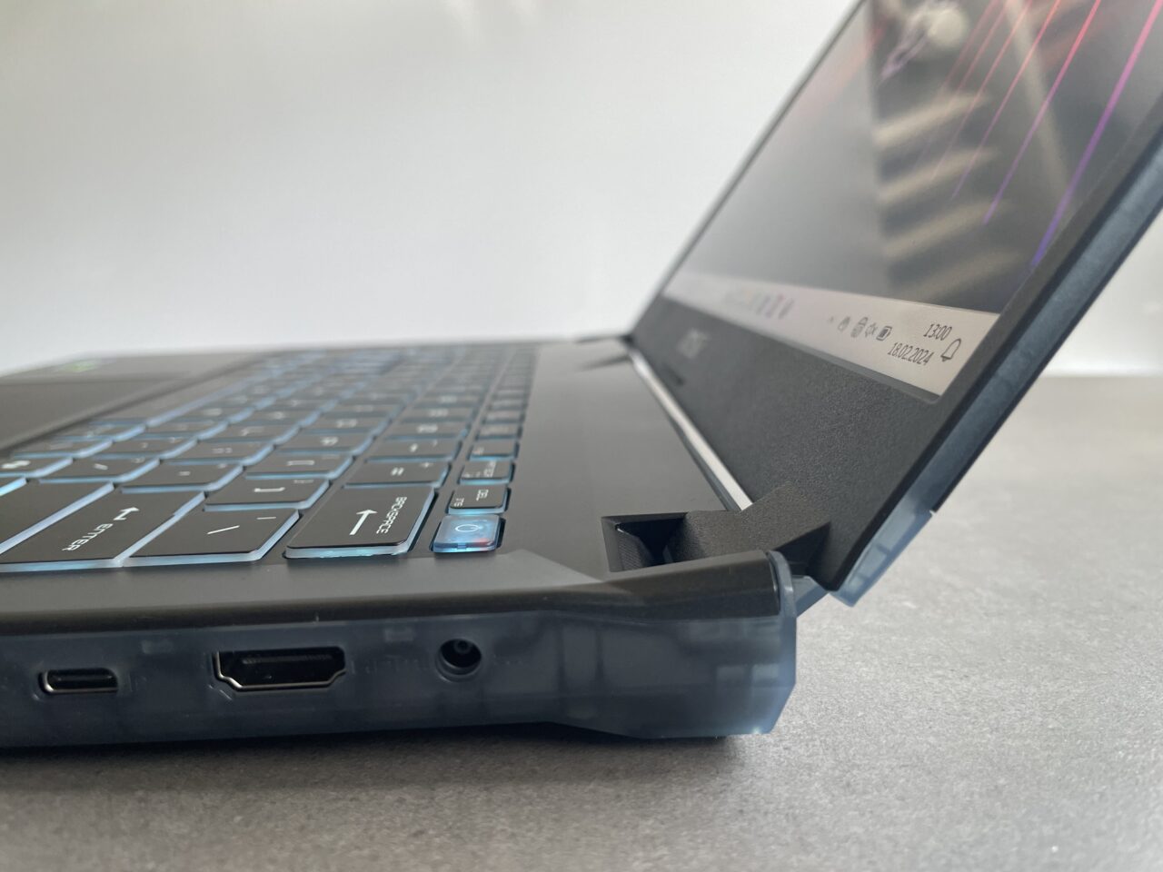 Częściowo otwarty laptop na szarym blacie z widoczną klawiaturą i portami po lewej stronie.