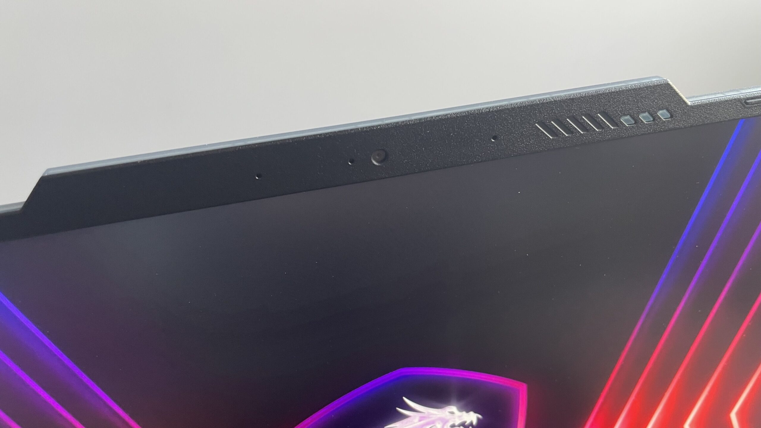Narożnik laptopa gamingowego z logo smoka na tle podświetlenia LED i wbudowaną kamerą internetową oraz mikrofonami u góry ekranu.