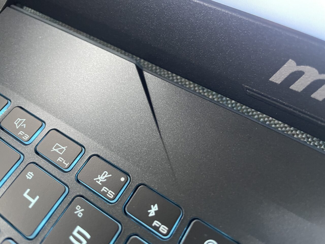Klawiatura laptopa z widocznym pęknięciem obudowy w pobliżu zawiasu.