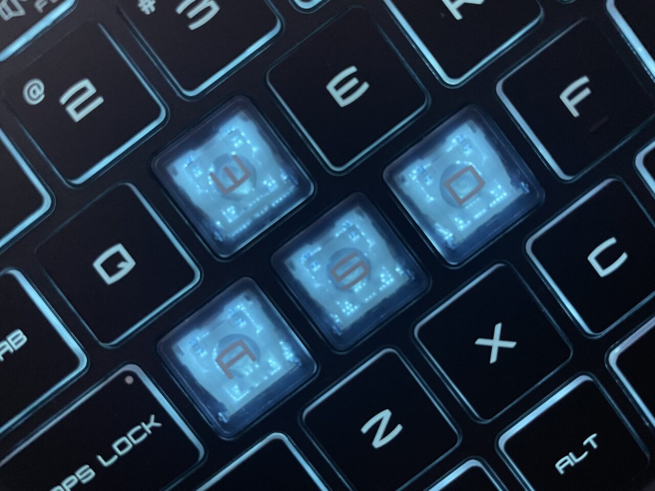 Klawiatura komputerowa z podświetlanymi klawiszami, w tym klawisze Caps Lock, A, S, D oraz częściowo widoczne klawisze z literami i symbolami wokół nich.