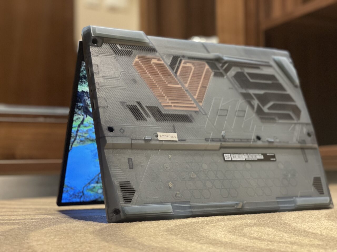 Laptop gamingowy umieszczony na płaskiej powierzchni, widoczny od spodu z otwartym ekranem w tle. Recenzja MSI Cyborg 14.