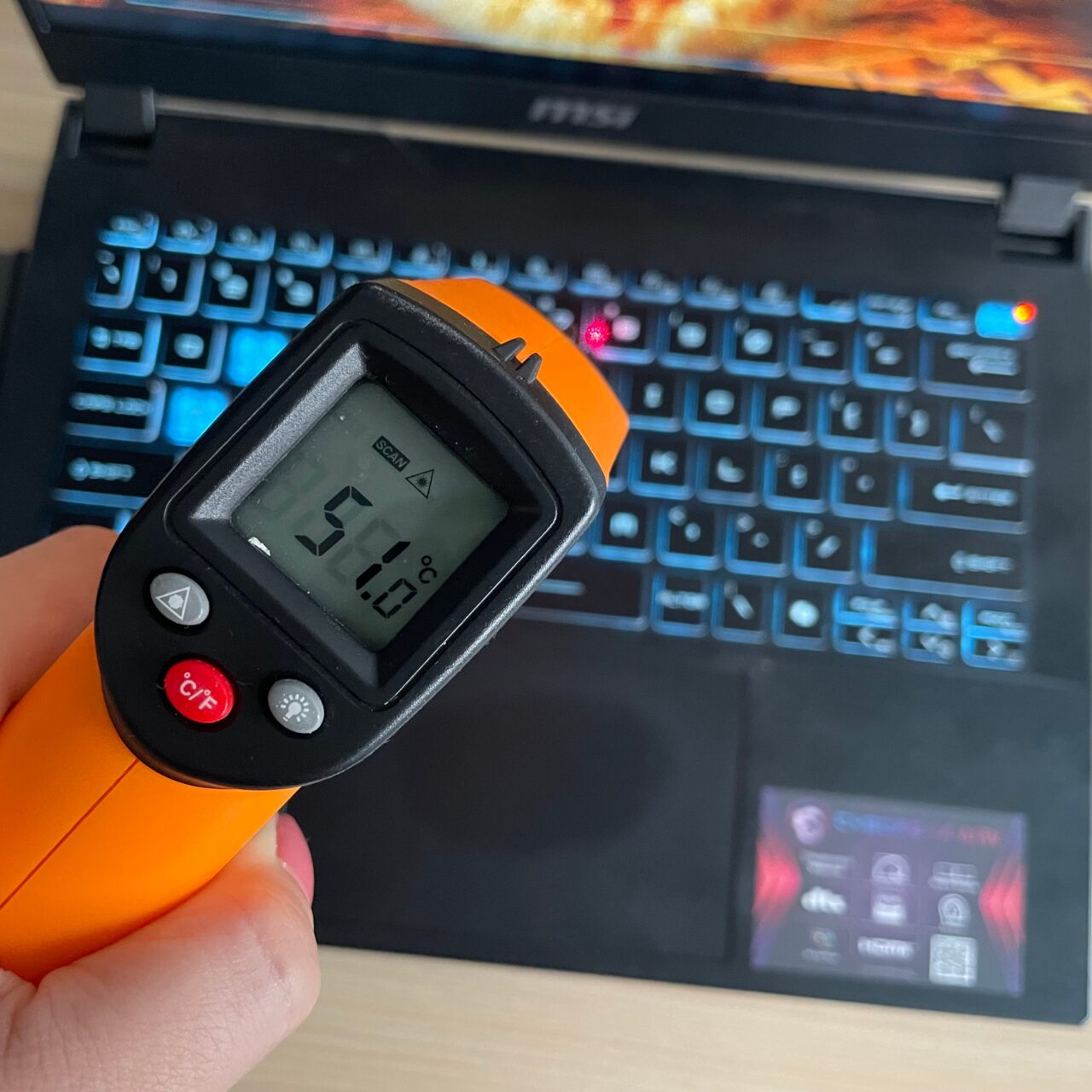 Cyfrowy termometr na podczerwień z pomiarem temperatury 51,5°C ukazujący klawiaturę laptopa w tle.